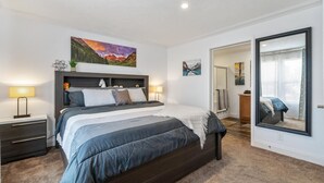 Une chambre à coucher avec un grand lit, des tables de chevet, une commode, un miroir et des œuvres d’art accrochées aux murs.