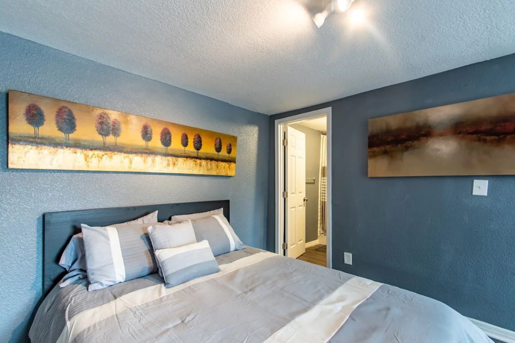 Une chambre à coucher avec un lit, un tableau accroché au mur et une porte donnant sur une autre pièce.