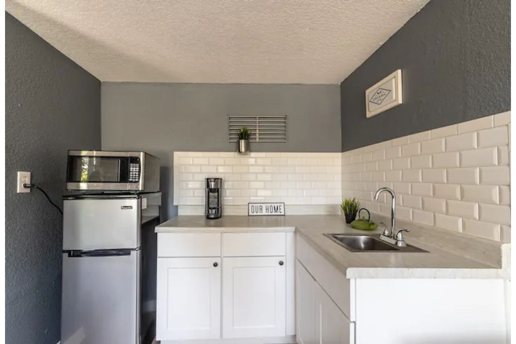 A compact kitchen with a microwave, refrigerator, white cabinets, a sink, and a 'OUR HOME' sign.