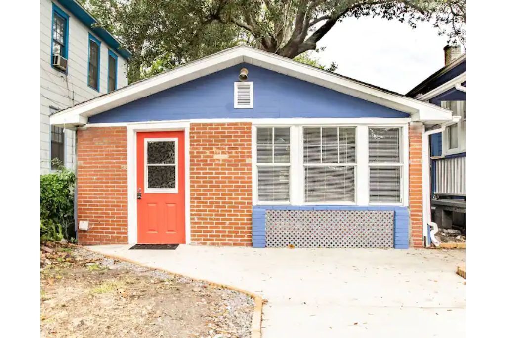 Una casa pequeña de un piso con puerta roja, techo azul y fachada de ladrillo.