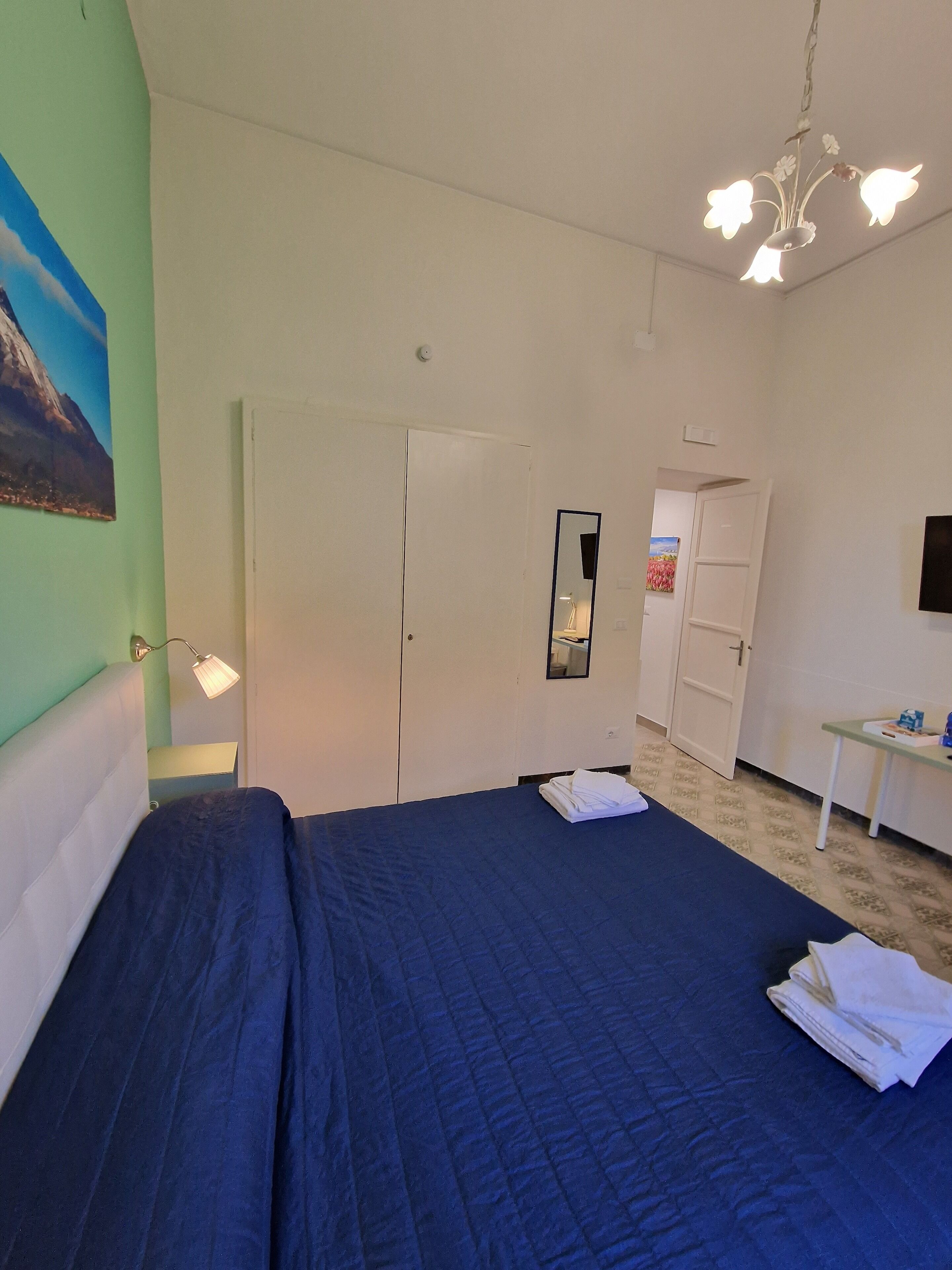 A bedroom with a bed, a nightstand, a mirror, and a door.