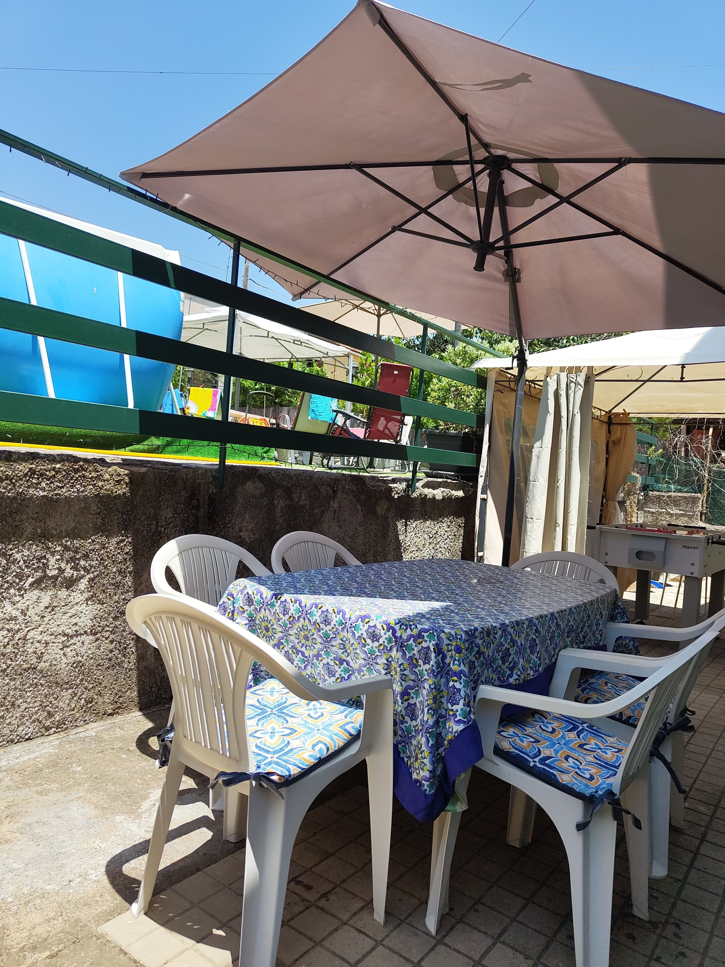 An outdoor patio with a table and chairs, a large umbrella, and a foosball table.