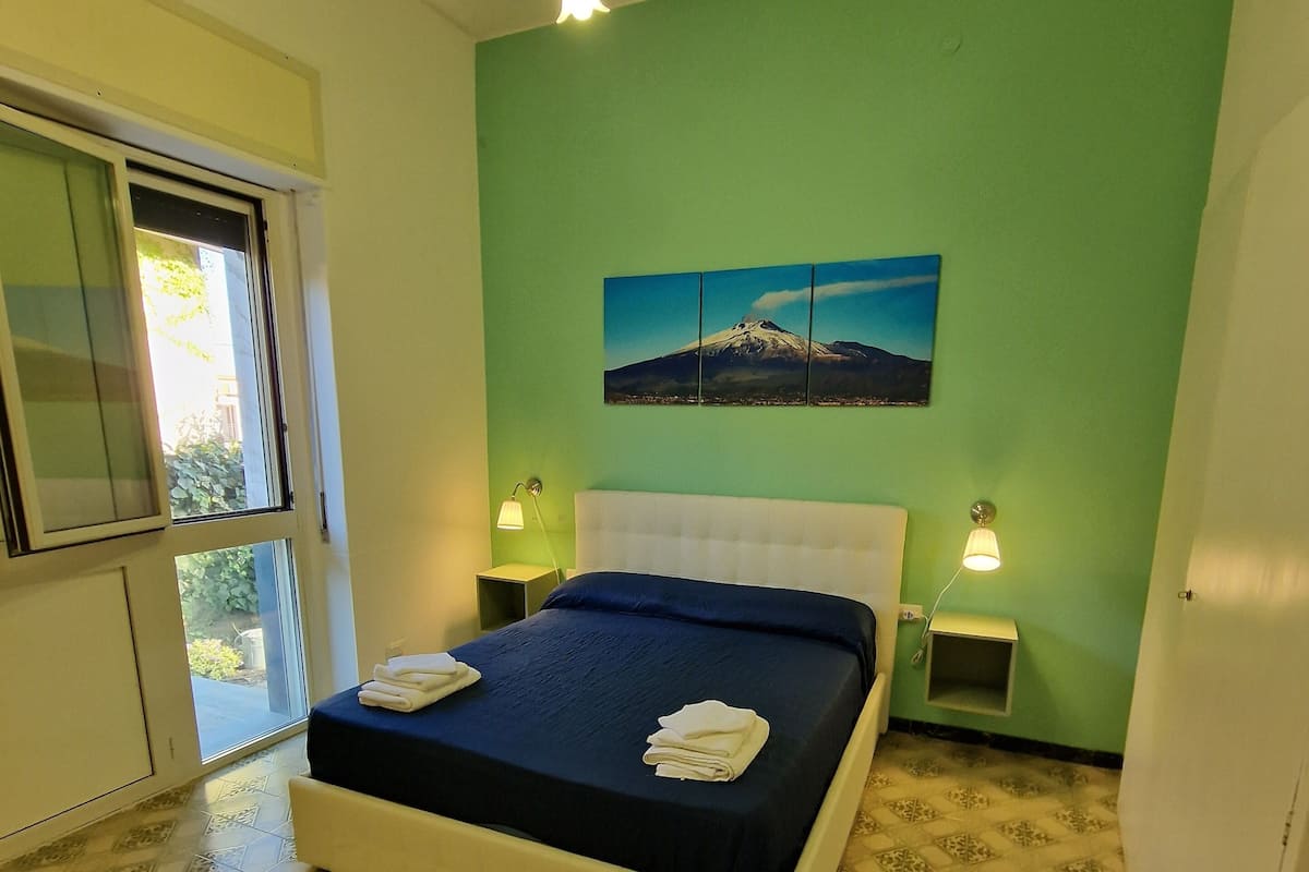 Une chambre à coucher avec un lit, deux lampes de chevet, une fenêtre et un tableau représentant une montagne.