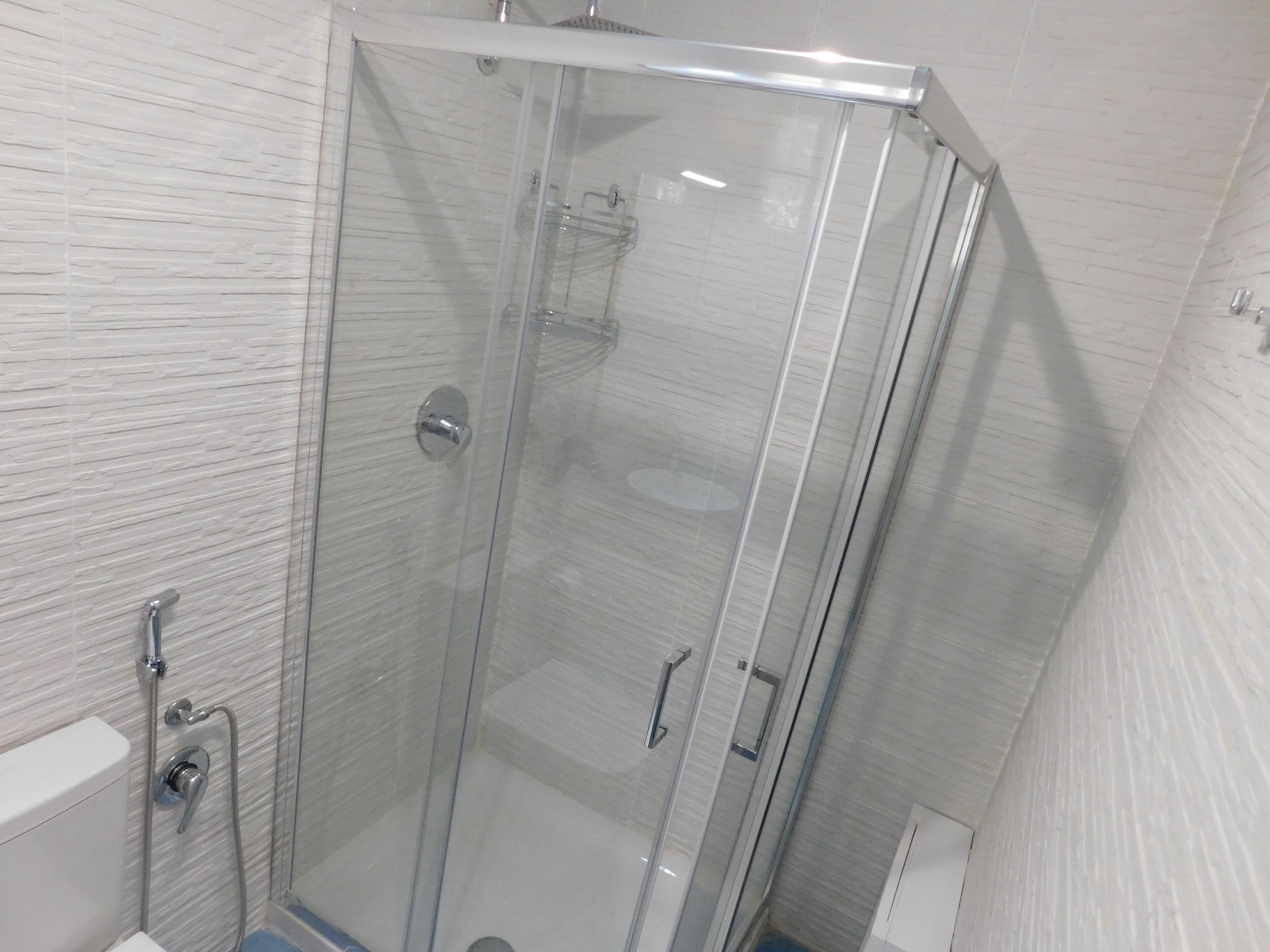 A glass-enclosed shower stall with a white tiled wall and a visible showerhead.