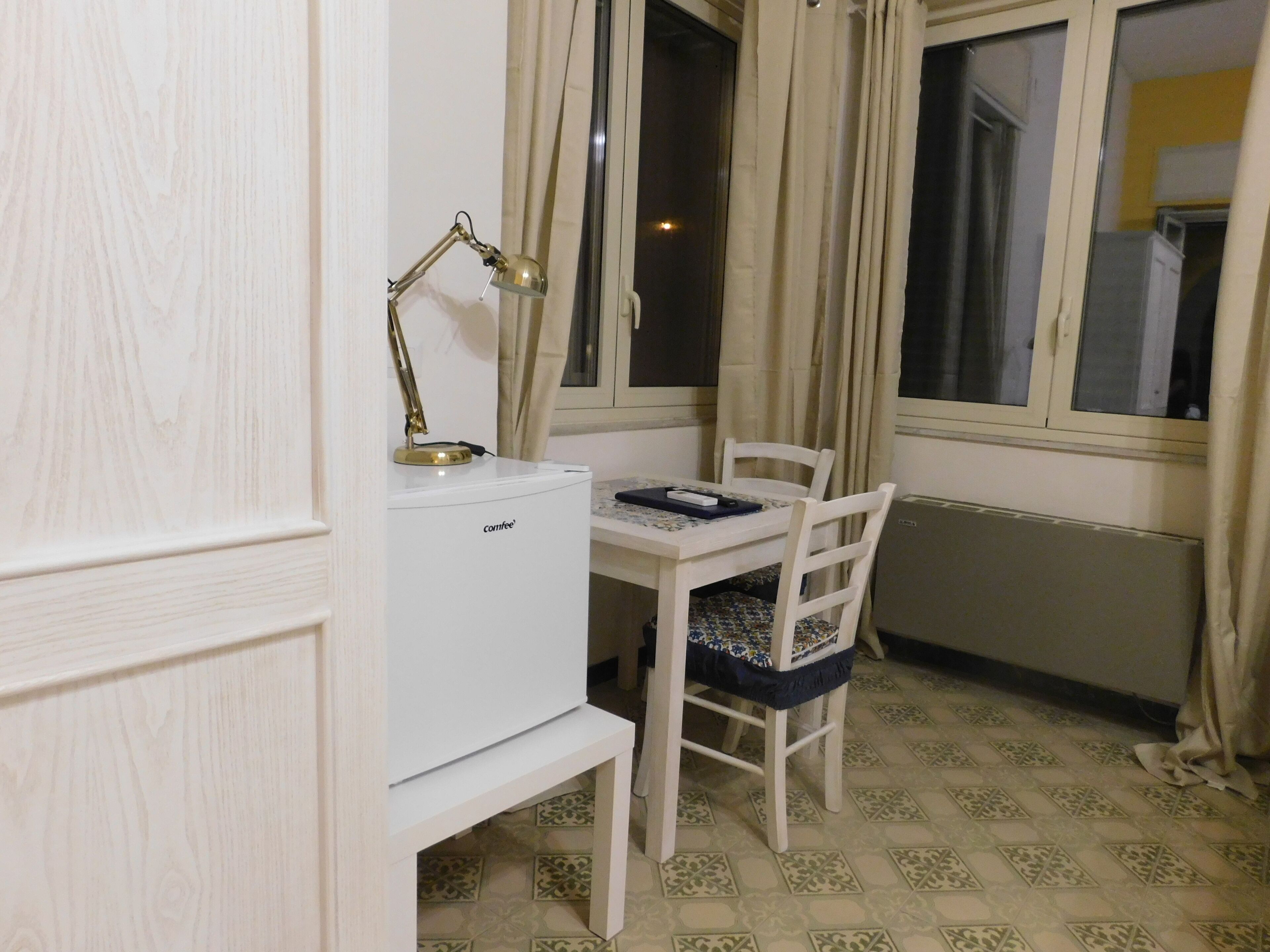A small, neatly arranged room with a white desk, a chair, a desk lamp, and a radiator.