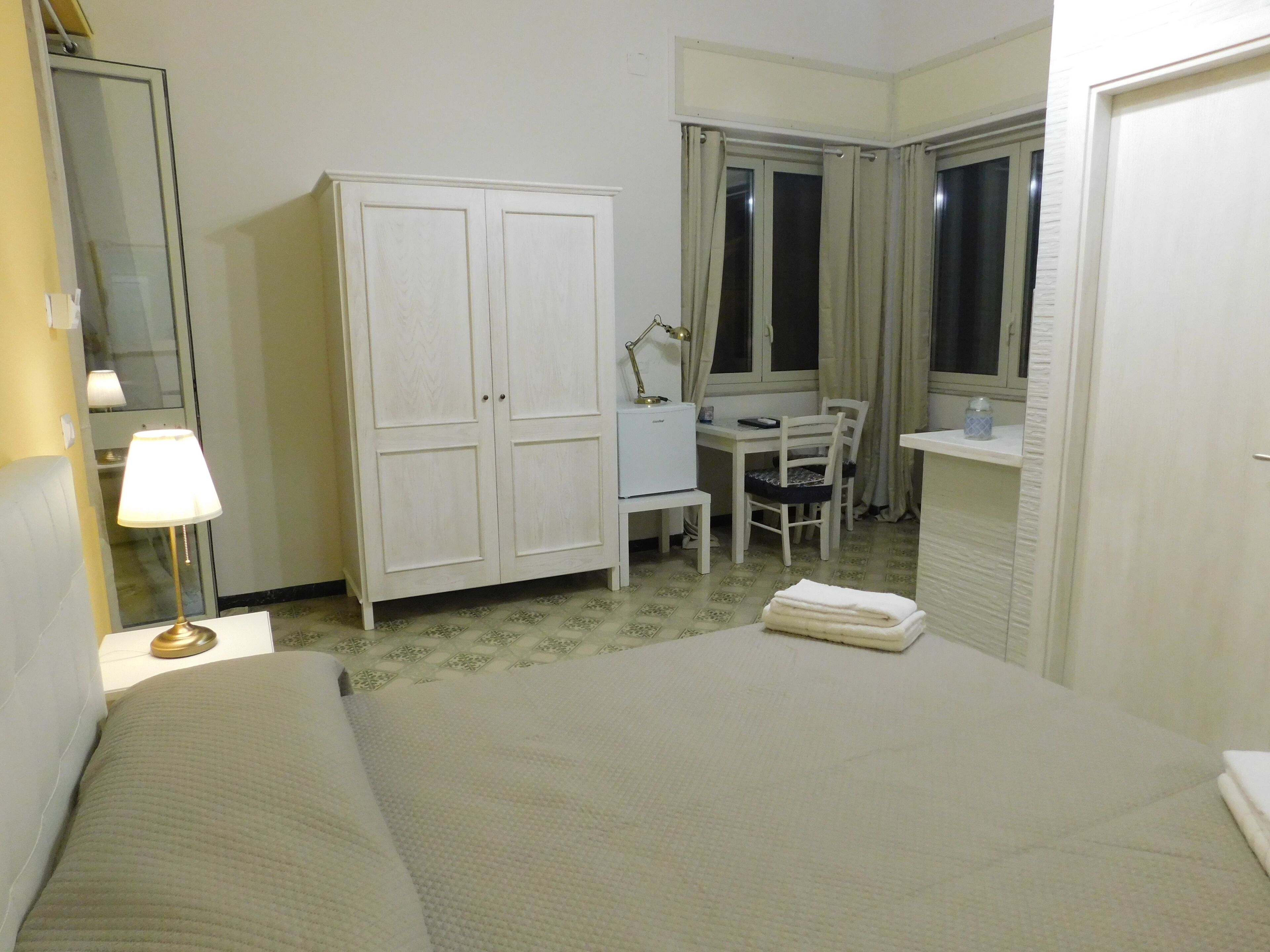 Habitació d'hotel amb llit, escriptori, cadira, armari i finestra amb cortines.