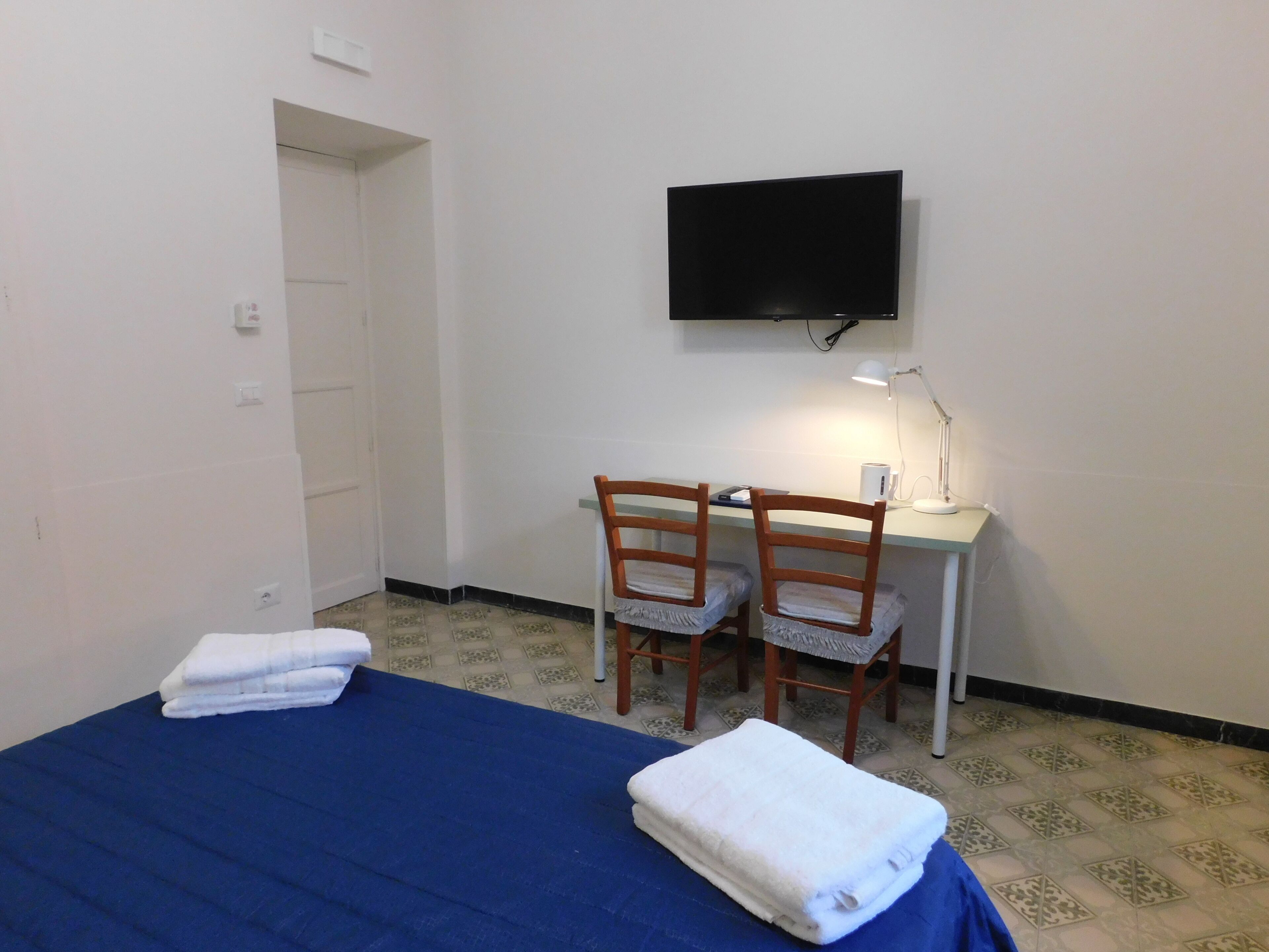 A room with a bed, two chairs, a desk, a TV, and a lamp.