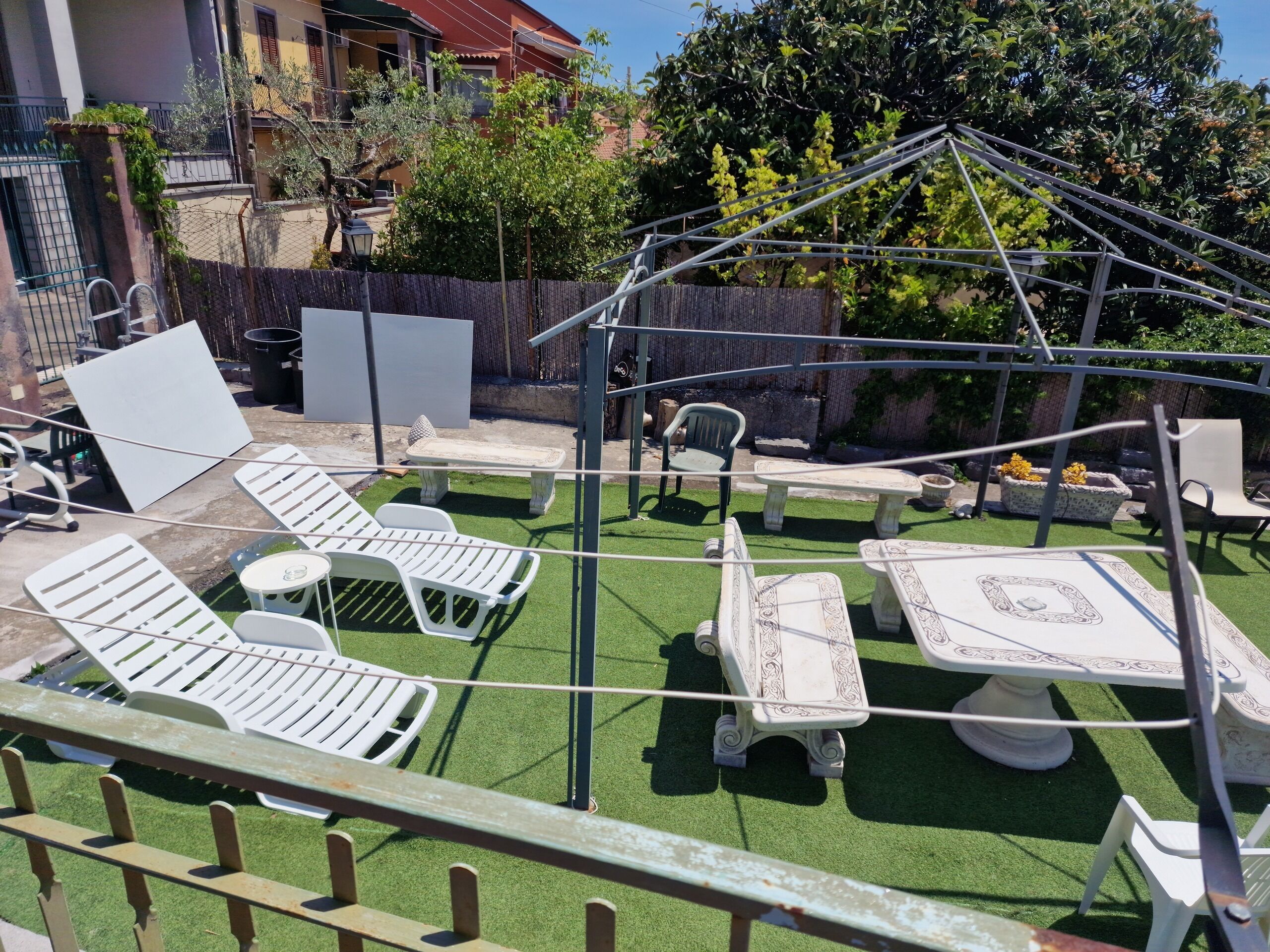 Een terras met buitenmeubilair, waaronder witte lounge fauteuils, een tafel en een kleine pergola.