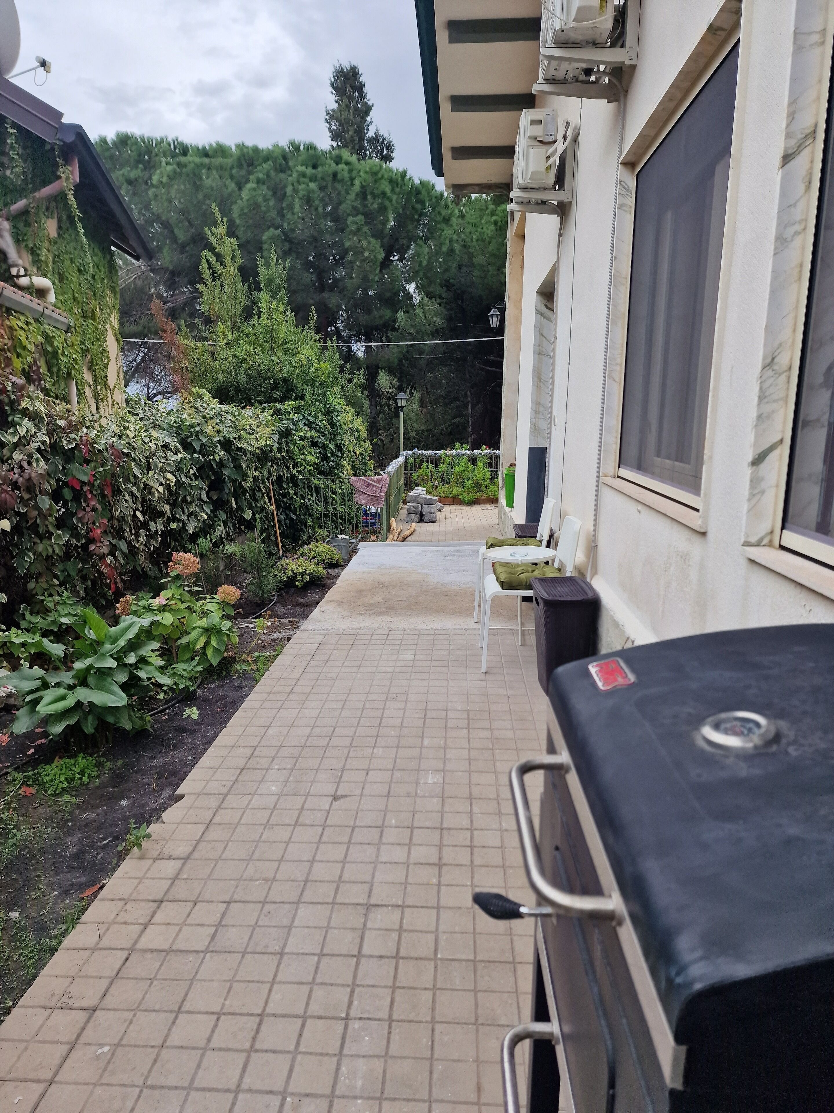 A patio area with a grill, outdoor seating, and a garden with various plants.