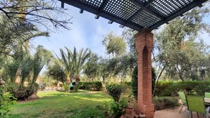 A patio area with a pergola, outdoor seating, and a garden with various plants and trees. - In the heart of Marrakech's Palmeraie (Marrakesh)