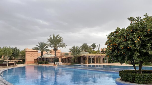 A swimming pool with tiled edges, surrounded by palm trees and a building with a traditional architectural style. - In the heart of Marrakech's Palmeraie (Marrakesh)