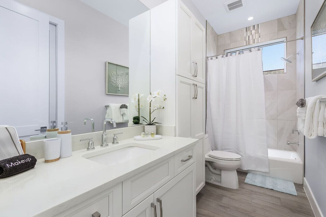 A modern bathroom with a large mirror, two sinks, a toilet, and a shower area.