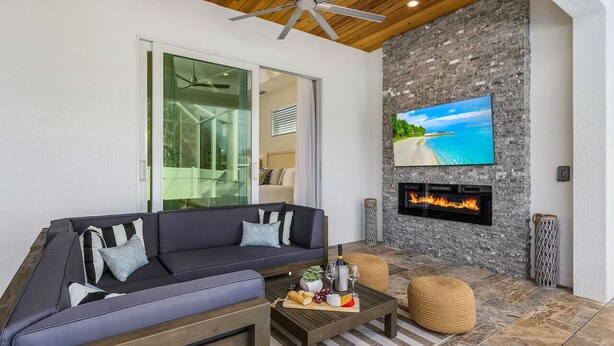 A modern outdoor living area with a stone wall, a flat-screen TV, a fireplace, and a sofa with cushions. - Serenity retreat * the ultimate luxury getaway (Naples)