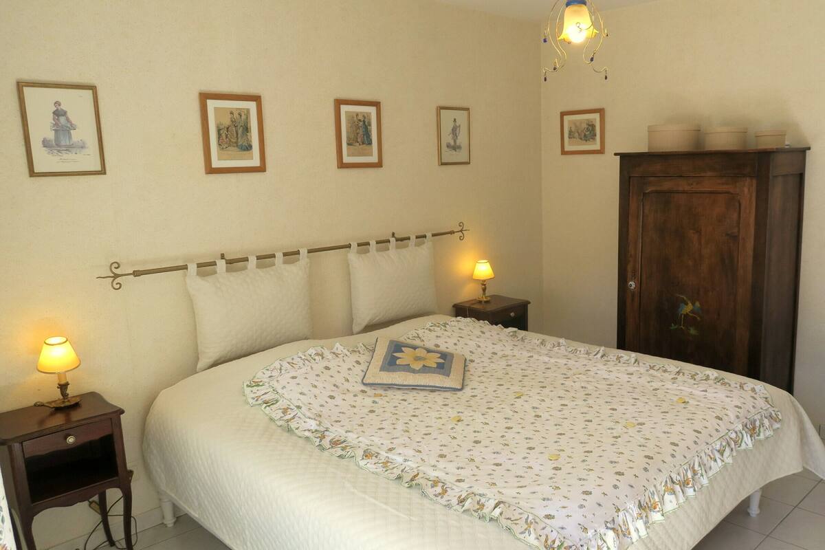 A bedroom with a bed, two bedside lamps, a wooden wardrobe, and a chair.