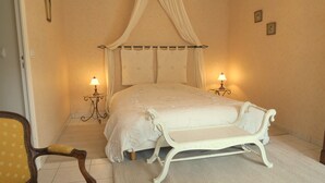 Ein Schlafzimmer mit einem Himmelbett, zwei Nachttischlampen, einer weißen Bank und einem Stuhl.