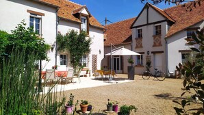 Ein Innenhof mit Tisch und Stühlen, umgeben von Gebäuden mit roten Ziegeldächern und weißen Wänden.