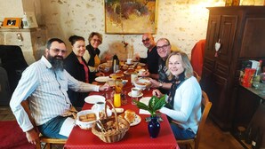 Eine Gruppe von Personen sitzt an einem Tisch mit verschiedenen Frühstücksangeboten in einem Raum mit rustikaler Wand und Holzschrank.
