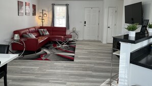 Un salon moderne avec un canapé rouge, une table basse en verre et un téléviseur posé sur un meuble noir.