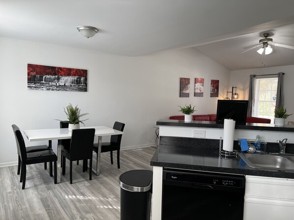 A modern kitchen with a dishwasher, sink, and a dining area with chairs and a table.