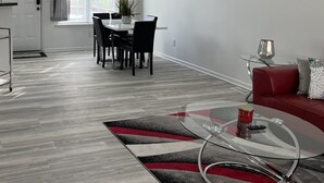 Un salon moderne comprenant un coin repas, un canapé rouge, une table basse en verre et un tableau accroché au mur.