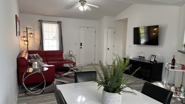 Un salon moderne avec un canapé rouge, une table basse en verre, une table à manger blanche et un ventilateur de plafond.