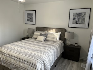 A neatly arranged bedroom with a large bed, two bedside tables with lamps, and two framed artworks on the walls.
