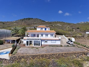 A two-story house with a swimming pool, a covered patio, and a car parked in front.