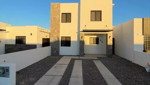 Um edifício residencial moderno de dois andares, com telhado plano, janelas amplas e entrada central.