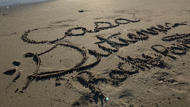 Uma praia com arte na areia e o sol brilhando.