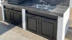 Uma cozinha externa com pia embutida e armários, churrasqueira e painel de backsplash de pedra.
