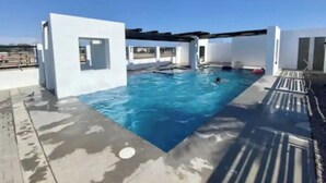 Piscina no terraço com água azul cristalina, rodeada por paredes brancas e um deck de concreto.