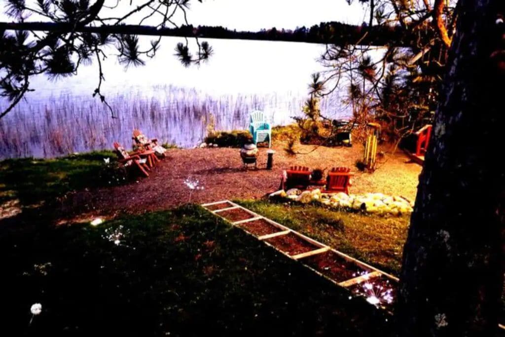 A lakeside outdoor seating area with a fire pit, a table, and chairs.
