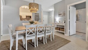 Zona pranzo con tavolo e sedie, un lampadario e una cucina sullo sfondo.