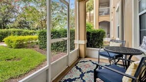 Una veranda coperta con tavolo e sedie, vista su un giardino curato e un edificio sullo sfondo.