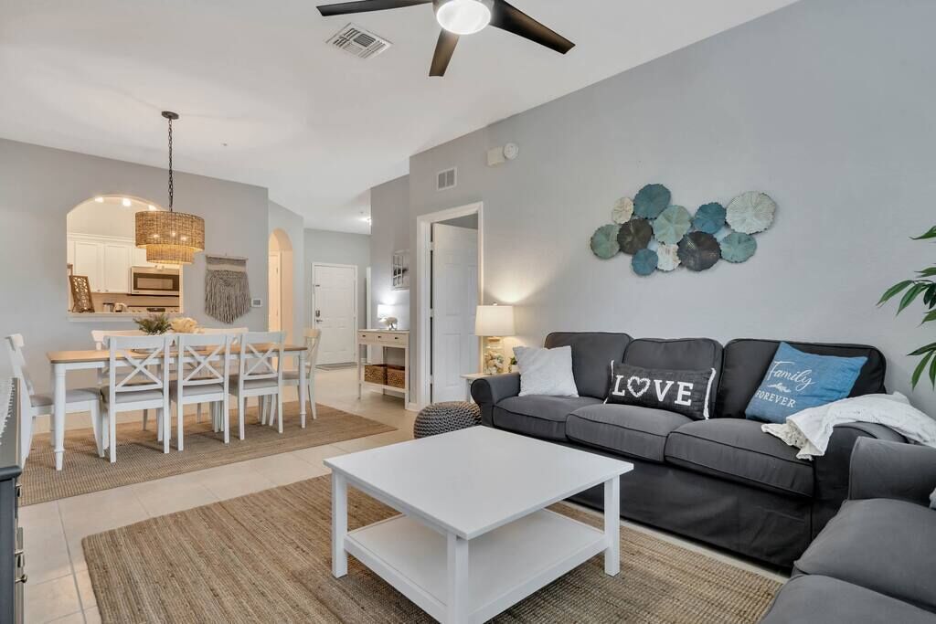 Een moderne woonkamer met een grijze bank, een witte salontafel en een eethoek met een witte tafel en stoelen.