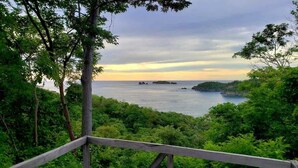 A coastal view with a wooden deck overlooking the sea, surrounded by lush greenery. - Steps to beach in the heart of Las Catalinas (Las Catalinas)