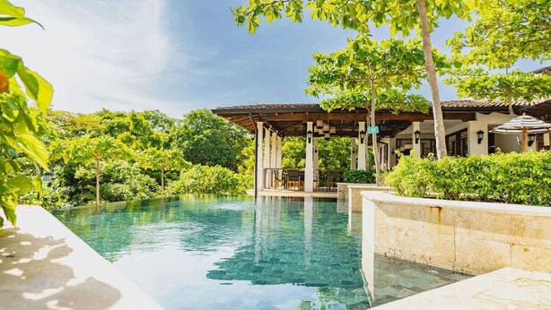 A clear swimming pool with a pergola and lounge area, surrounded by lush greenery and a traditional building. - Steps to beach in the heart of Las Catalinas (Las Catalinas)