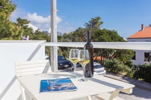 Uma mesa branca com uma garrafa e duas taças de vinho branco, um folheto, e vista para uma área residencial com carros e árvores.