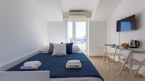 A hotel room with a bed, a desk, a chair, a TV, and a view of the sea.