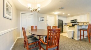 A dining area with a round table and chairs, a kitchen with white cabinets, a refrigerator, and a microwave.