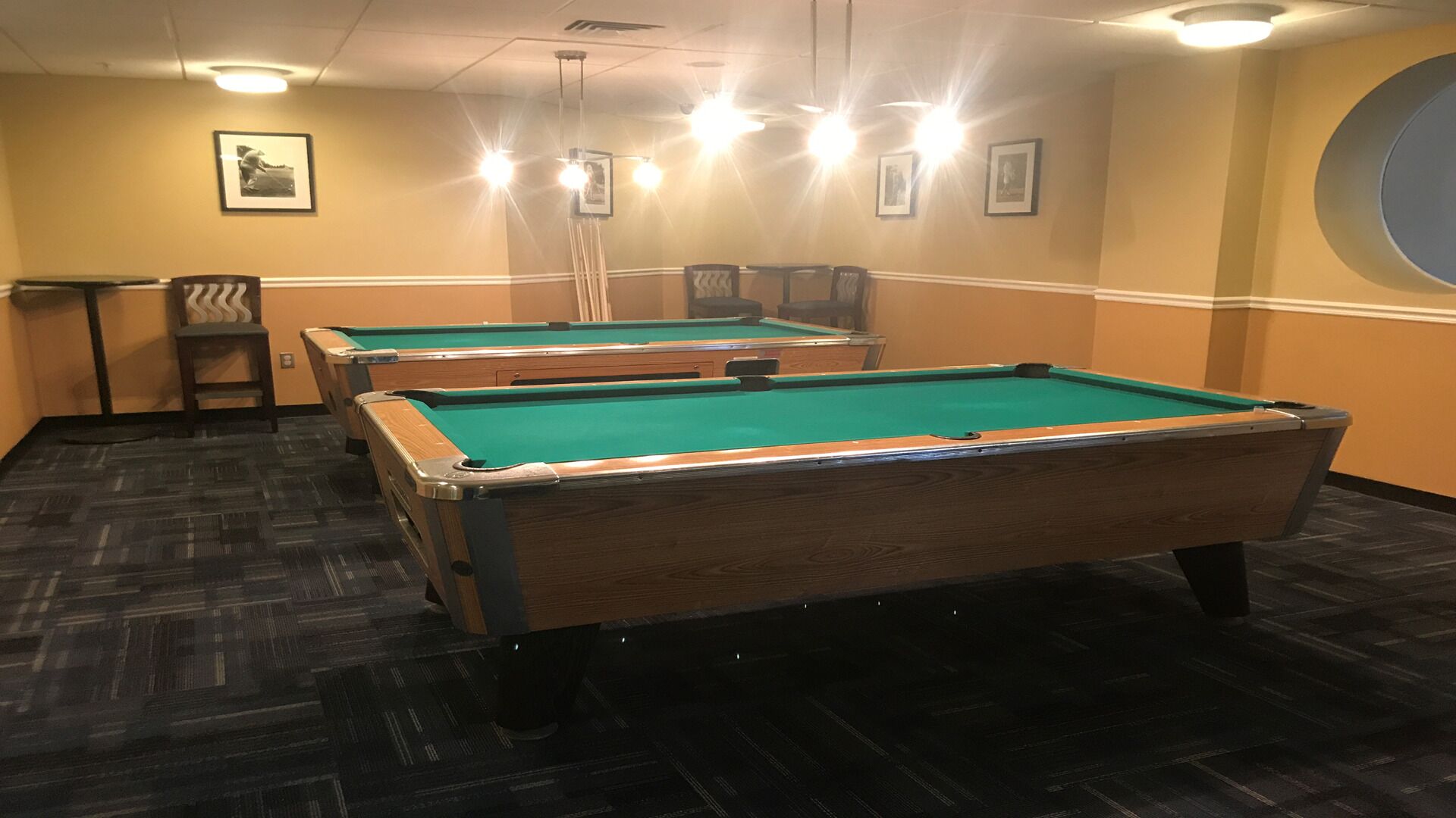 A pool table area with two pool tables, a small table with chairs, and framed pictures on the wall.