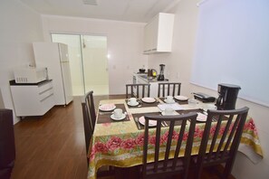 A dining area with a table set for four, chairs, a microwave, and a refrigerator in the background. - MORADA PINHEIRO (Bombinhas)
