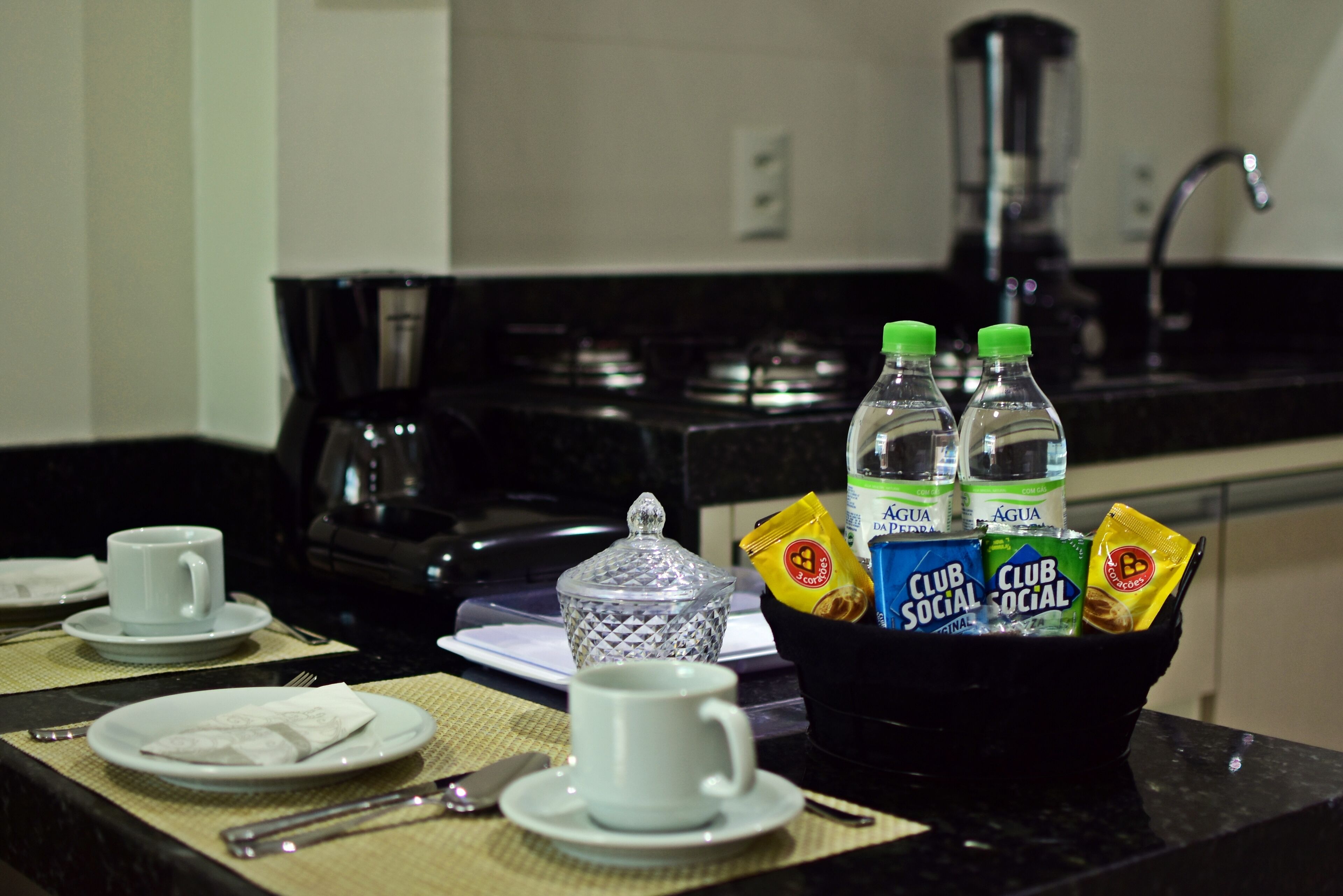 A kitchen with a coffee maker, two bottles of water, and packets of snacks on the counter.