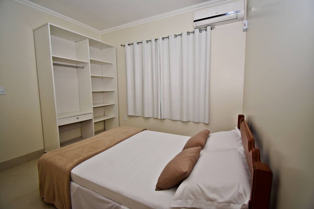 Une chambre à coucher avec un lit, une tête de lit en bois, une armoire et une fenêtre avec des rideaux.