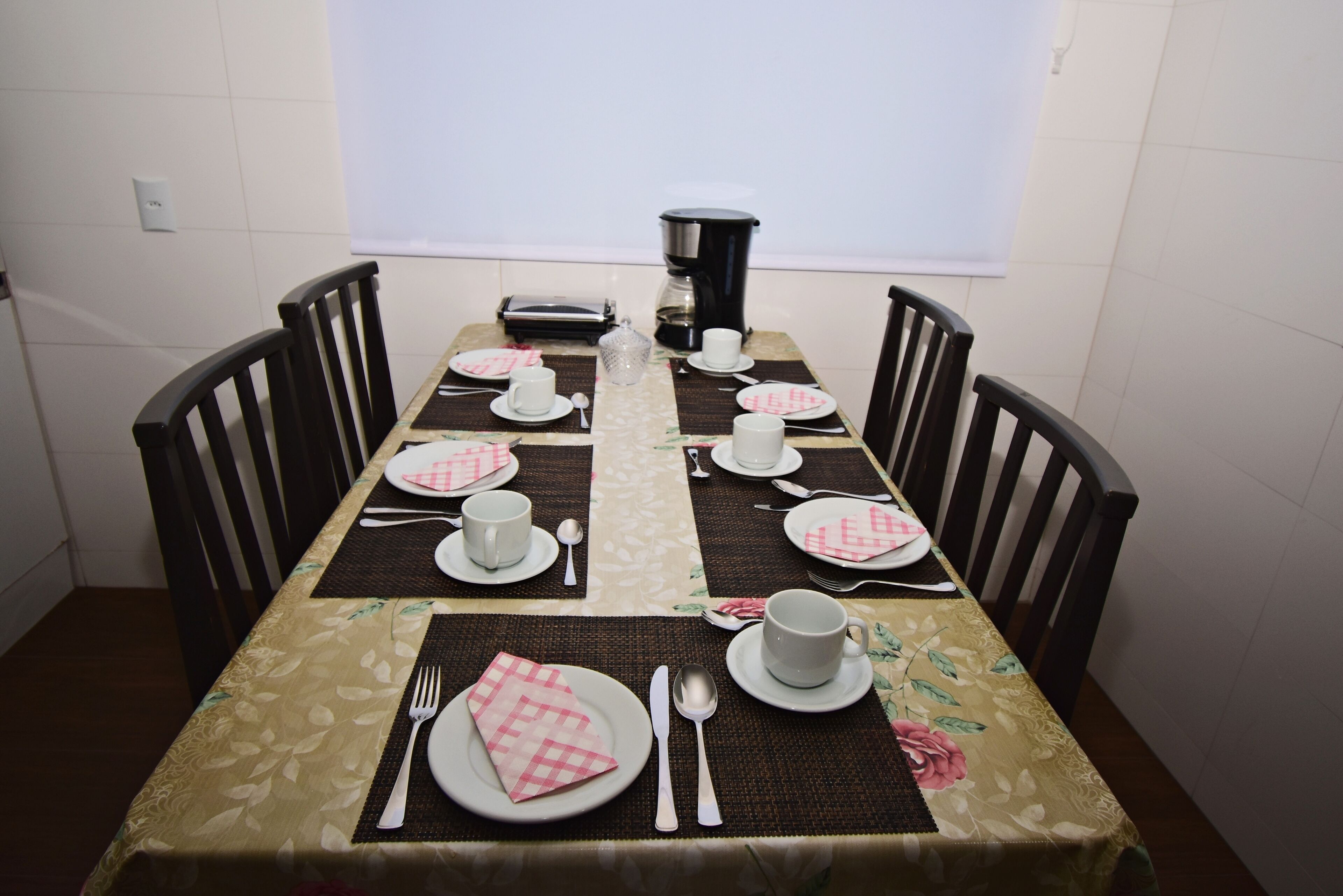A dining table set for four with a coffee maker, plates, cups, and cutlery.