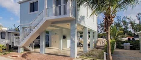 A two-story house with a balcony, a covered porch, and a palm tree in the background.