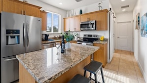 A modern kitchen with granite countertops, stainless steel appliances, wooden cabinets, and a large window providing natural light. - Key Largo home with new hot tub! (Key Largo)