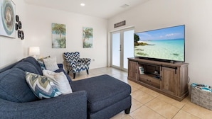 A living room with a large flat-screen TV, a sofa, a patterned armchair, and a wooden entertainment unit. - Key Largo home with new hot tub! (Key Largo)
