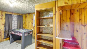 Una habitación con paredes de madera, una estantería de piedra, una mesa de fútbol y un banco rojo.