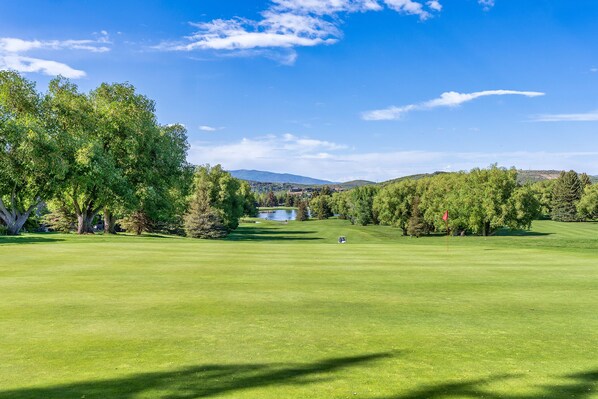 En golfbane med en sø, træer og et fjerntliggende bjerglandskab.